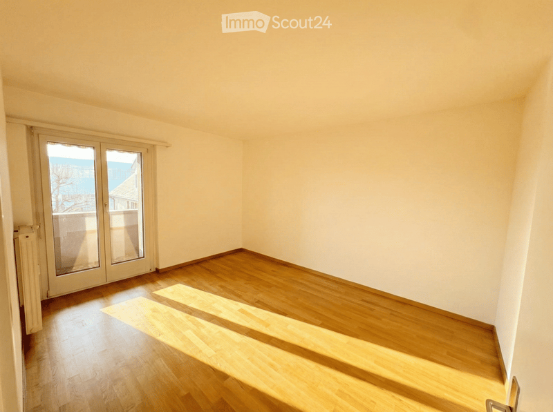 Empty room with wooden flooring and large glass sliding doors leading to a balcony.