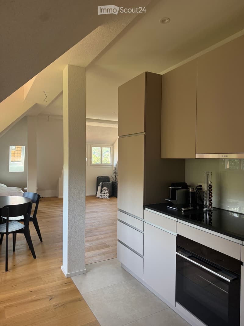Modern kitchen with white cabinets, black countertops, and stainless steel appliances. Adjacent dining area with wooden flooring and black chairs around a round table.