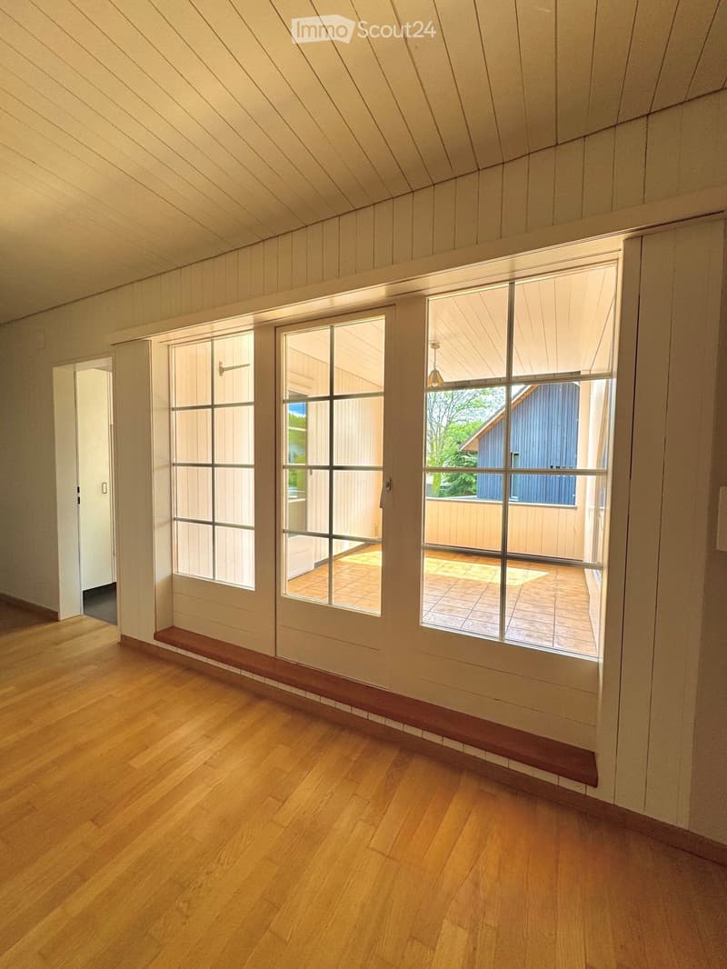Empty room with wooden flooring, white walls, large windows, and a door leading to an outdoor area.