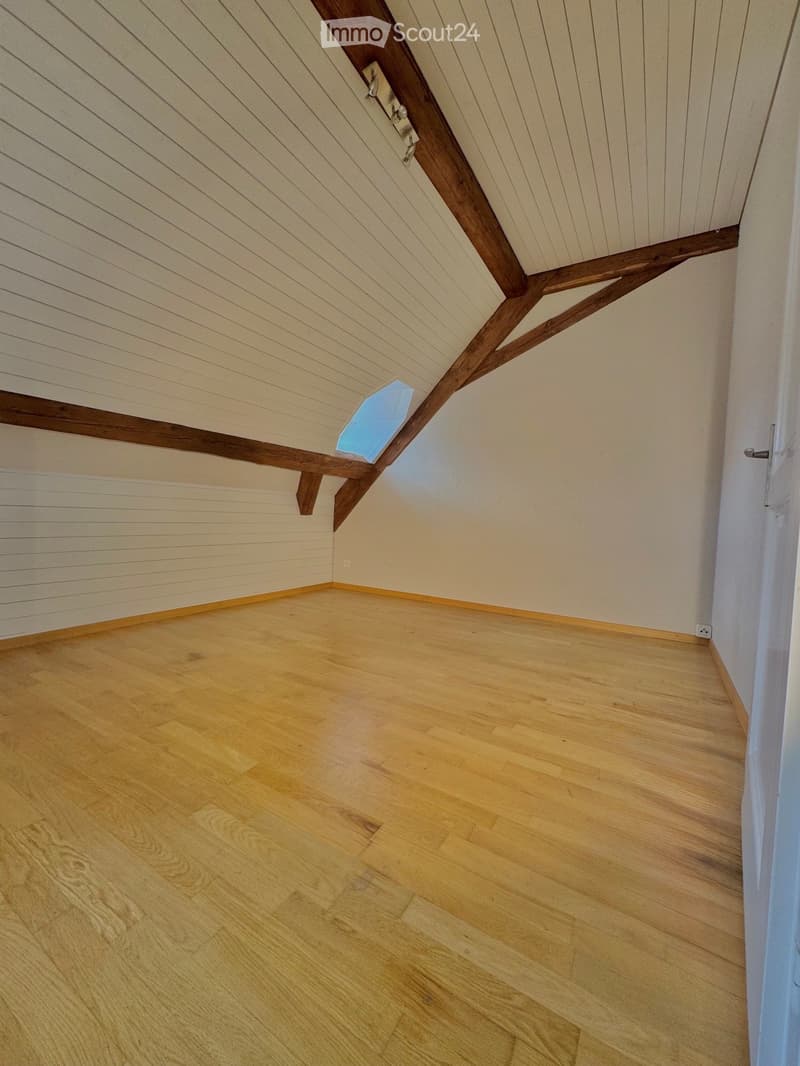 Empty attic room with wooden floor, white walls, and exposed wooden beams on the ceiling. Features a skylight window and a door.