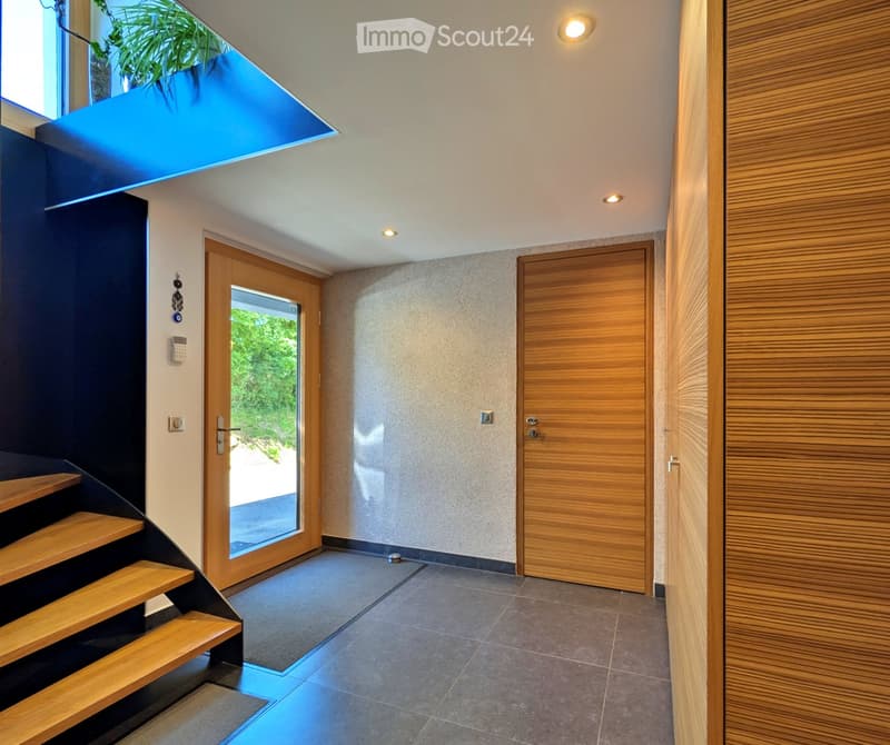 Modern hallway with wooden stairs, glass door, and recessed lighting. Features a sleek design with a combination of dark and light tones.