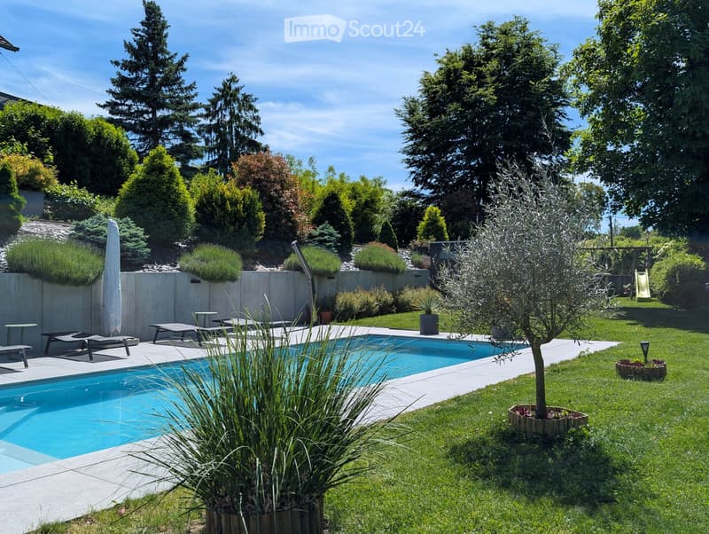 Well-maintained garden with a swimming pool, lounge chairs, a small table, and various plants and trees.