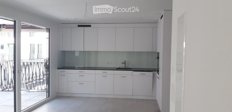 Modern, minimalist kitchen with white cabinets, a central island, and a sleek glass backsplash. Features a large sliding glass door leading to a balcony.