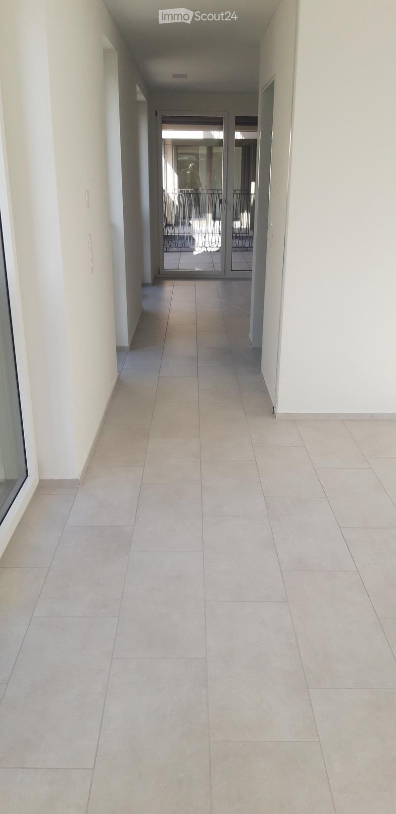 Clean, modern hallway with tiled flooring and white walls, leading to a glass door opening onto a balcony area.
