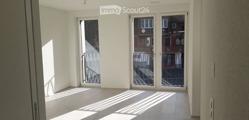 Empty room with white walls, tiled floor, and large sliding glass doors leading to a balcony with metal railings.