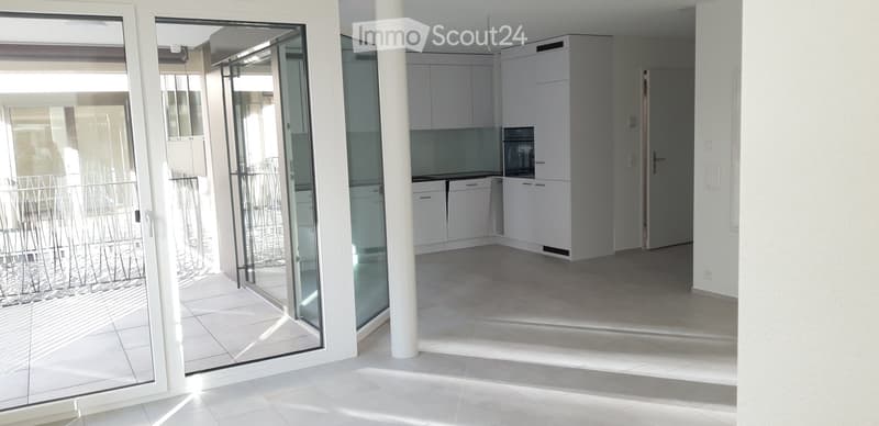 Empty kitchen with white cabinets, a microwave, and a tiled floor, connected to a balcony through large glass doors.