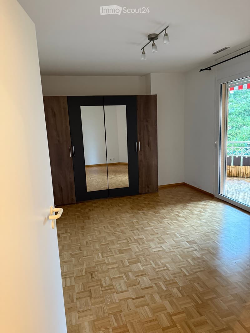 Empty room with wooden herringbone flooring, large mirrored wardrobe, and sliding glass door leading to a balcony.