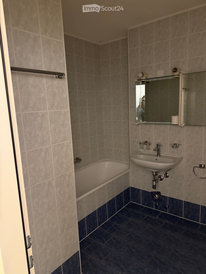Bathroom with a bathtub, sink, mirror, and dark tiled floor.