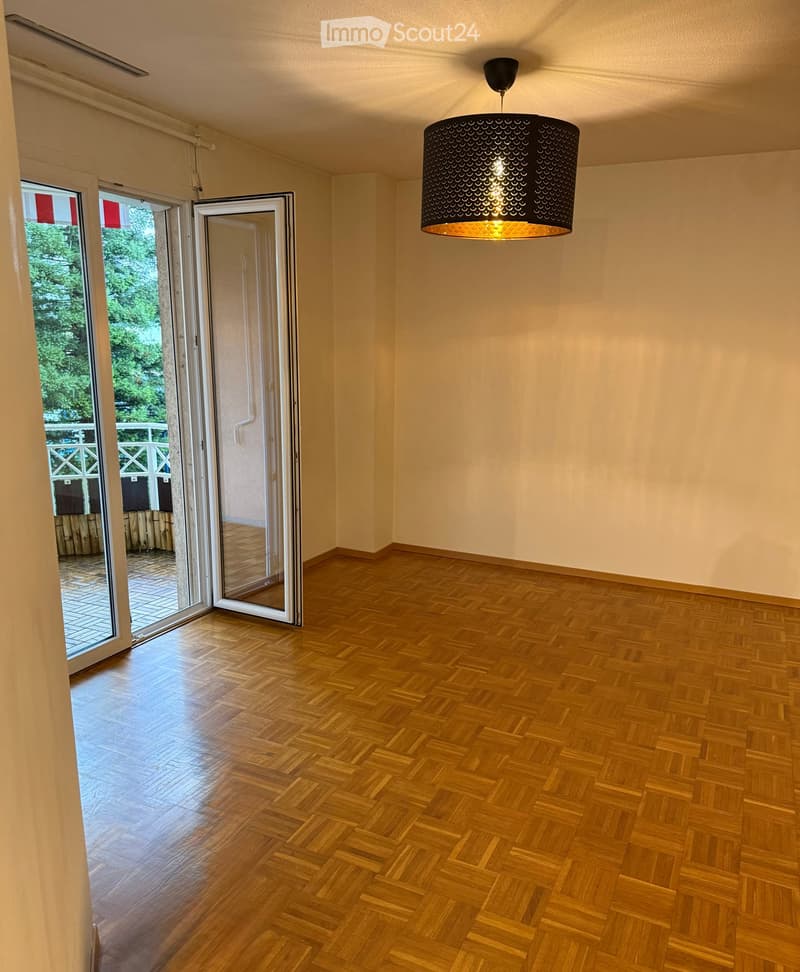 Empty room with wooden herringbone flooring, large sliding glass doors leading to a balcony, and a modern pendant light fixture.