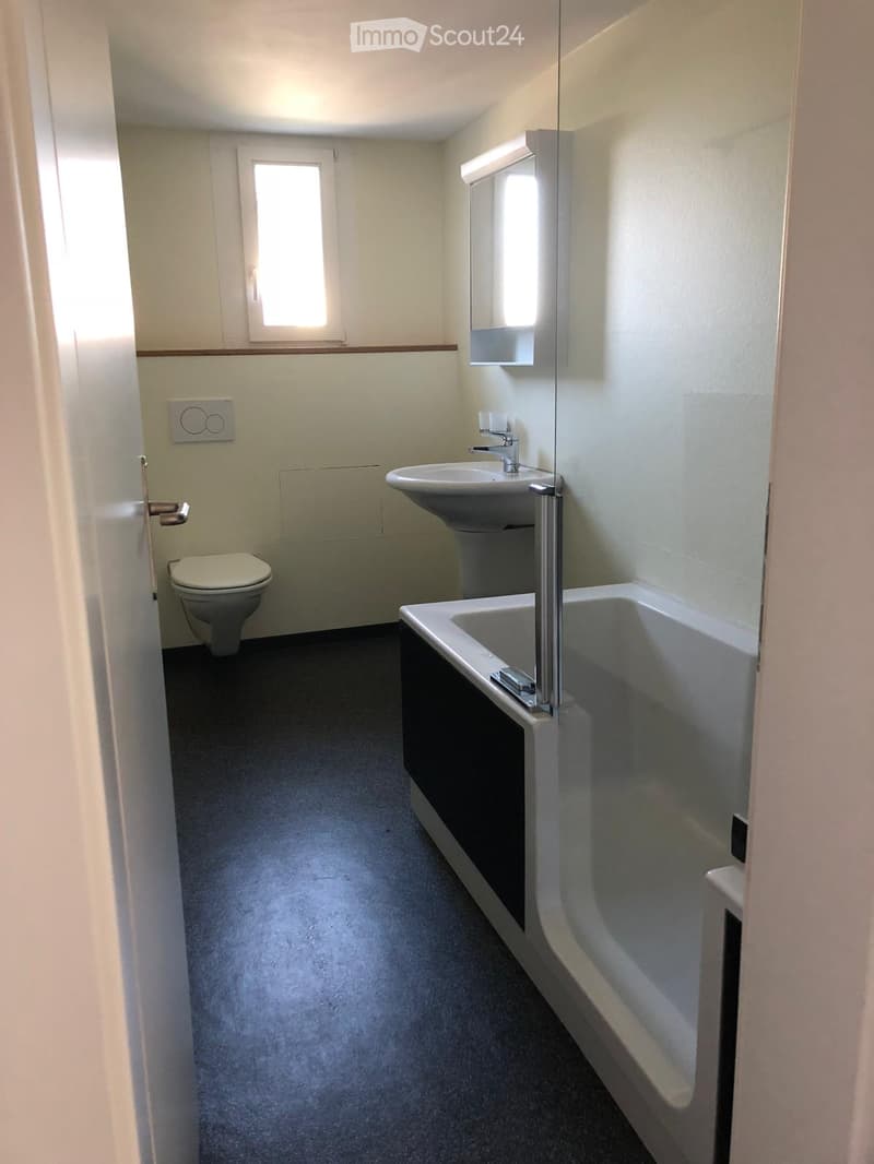 Modern bathroom with a toilet, sink, bathtub, and mirror. Light-colored walls and dark flooring.