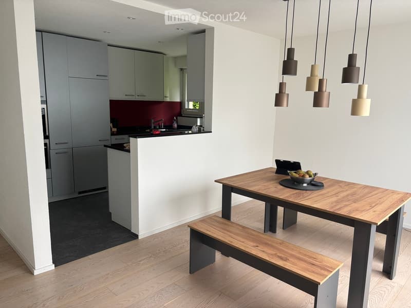 Open-plan kitchen and dining area with modern grey cabinets, a wooden dining table with bench seating, and pendant lights.