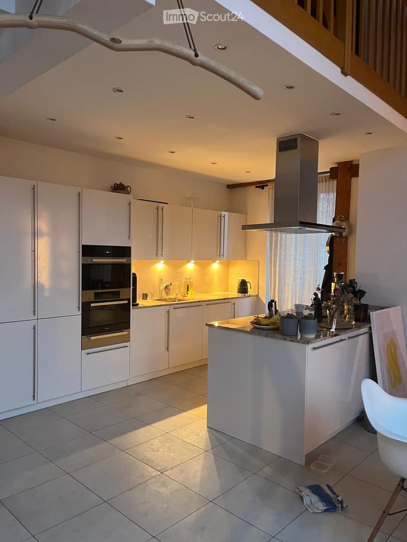 Modern kitchen with white cabinets, stainless steel appliances, a central island, and a staircase leading to an upper level.