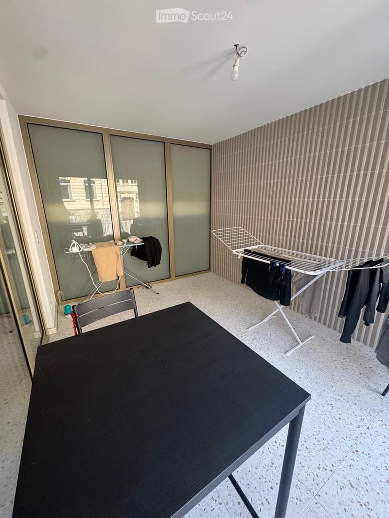 Balcony with a black table, a chair, an ironing board, and a clothes drying rack with hanging clothes.