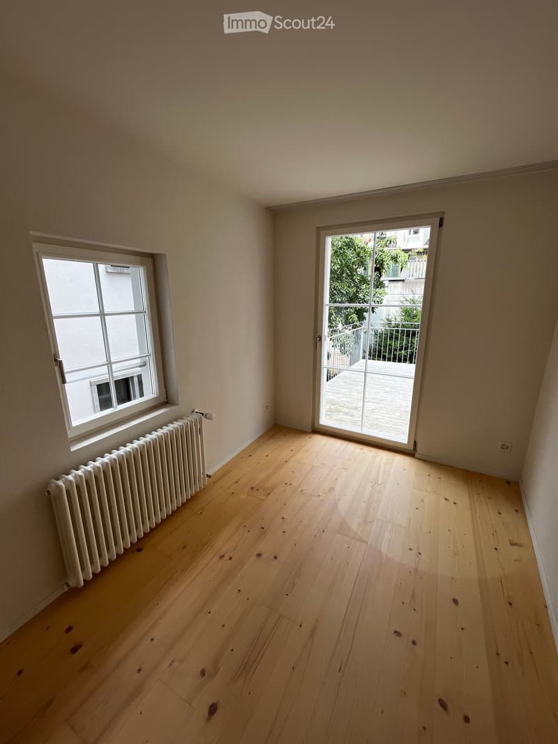 Empty room with wooden flooring, white walls, a radiator, and a sliding glass door leading to a balcony.