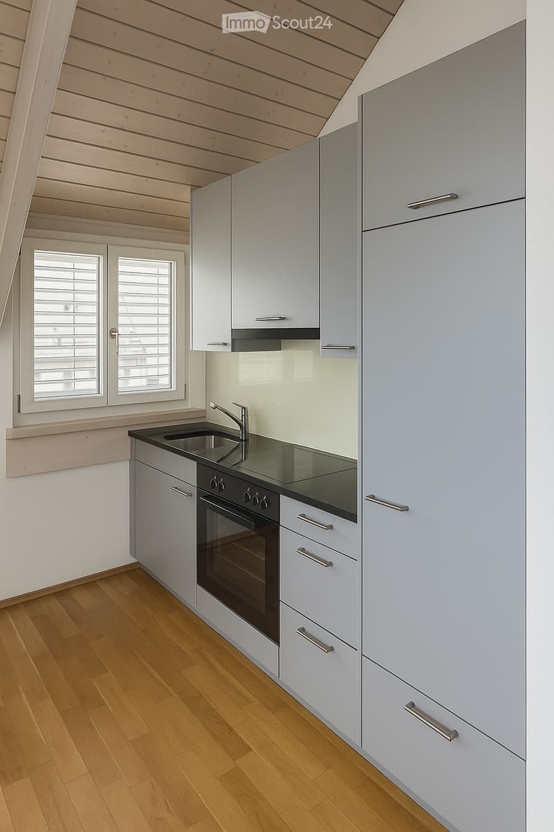 Modern kitchen with light grey cabinets, wooden flooring, and a sleek black countertop featuring a sink and oven.