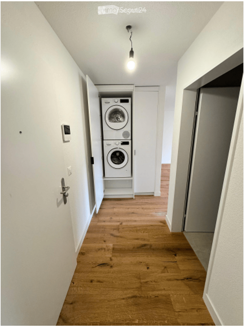 Hallway with wooden flooring, white walls, and a built-in laundry area containing a washing machine and dryer.