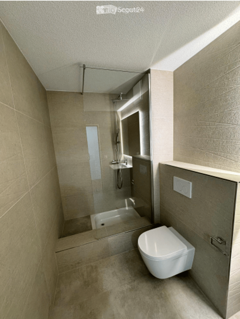 Modern, minimalist bathroom with light beige tiles, a toilet, a shower area with glass enclosure, and a sink.