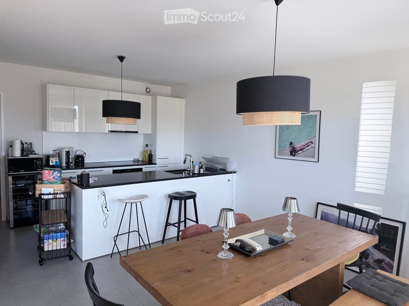 Modern kitchen and dining area with white cabinets, black countertops, a wooden dining table, and various appliances.
