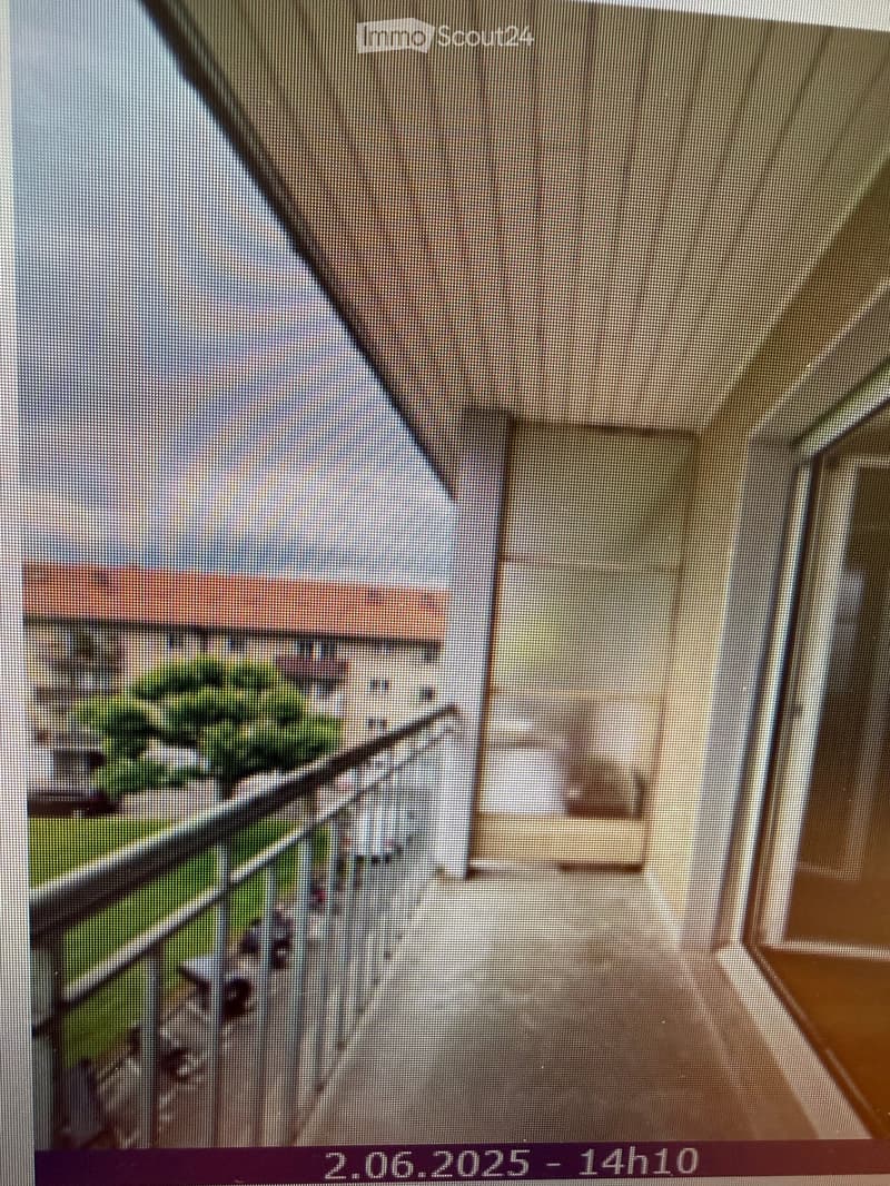 A view from inside a room looking out onto a balcony or terrace area with outdoor furniture and greenery visible beyond.