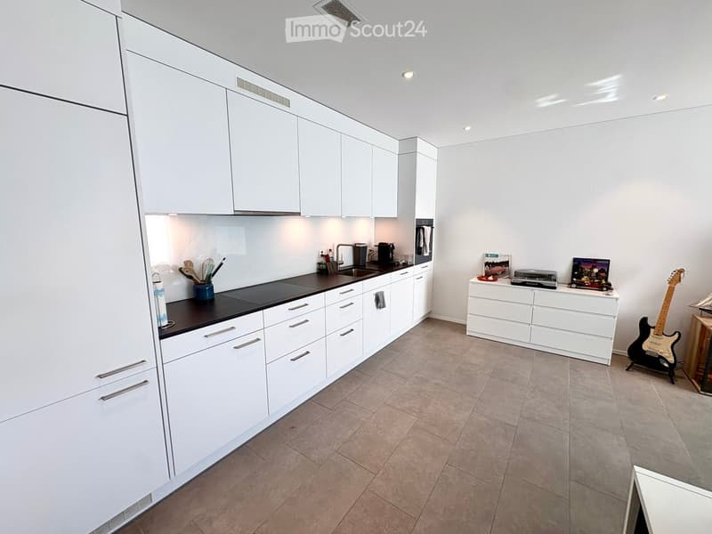 Modern kitchen with white cabinets, black countertops, and various appliances. Includes a sink, coffee maker, and a guitar on display.