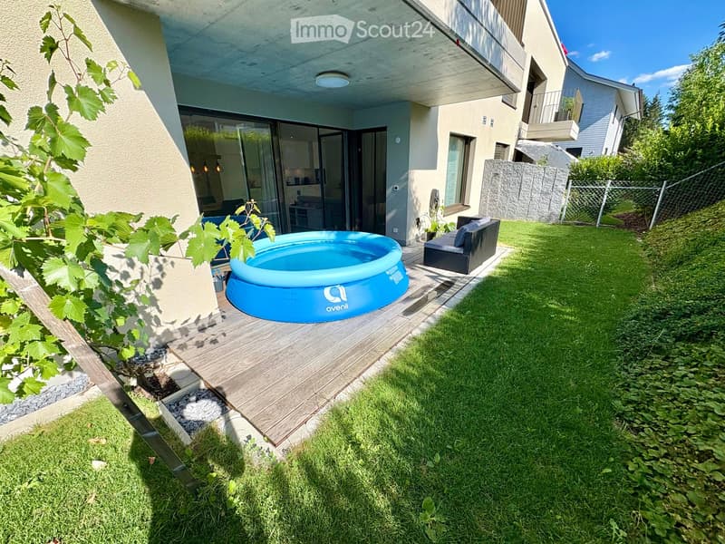 Garden with a wooden deck, inflatable pool, lounge chair, and surrounding greenery.