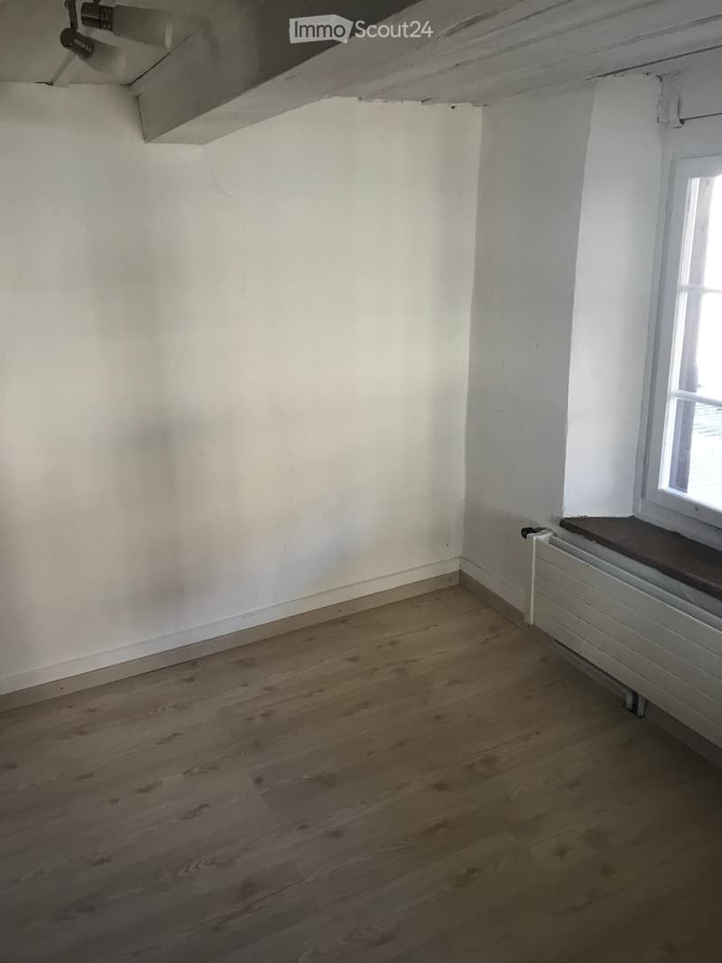 Empty room with wooden flooring, white walls, and a single window with a radiator below it.