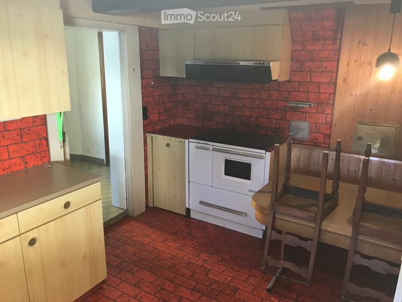 Kitchen with red brick walls, wooden cabinets, stove, oven, and a small dining area with a table and chairs.
