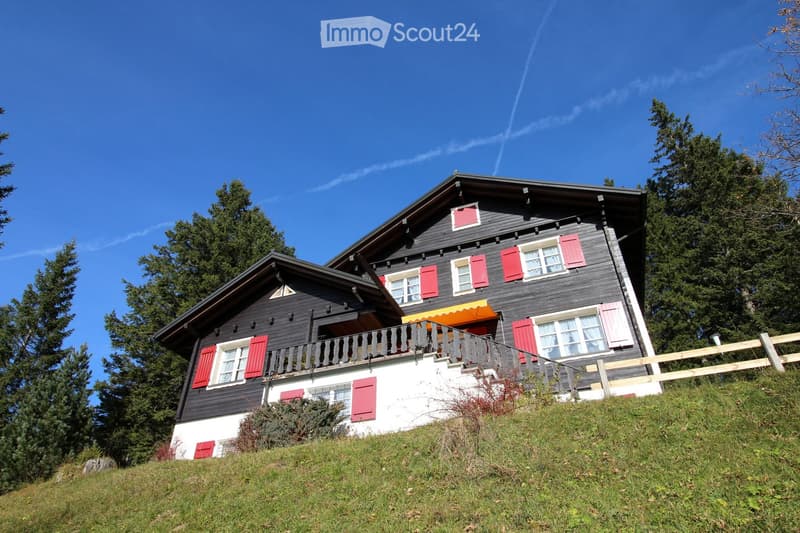 Two-story house with dark wooden exterior, red shutters, white lower section, and a balcony with an orange awning.
