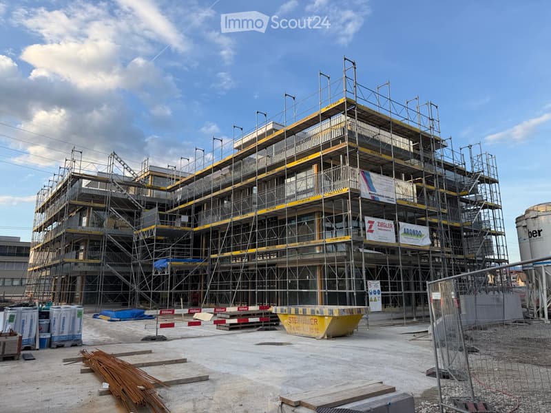 Multi-story building under construction with scaffolding, visible signage, and construction materials on the ground.