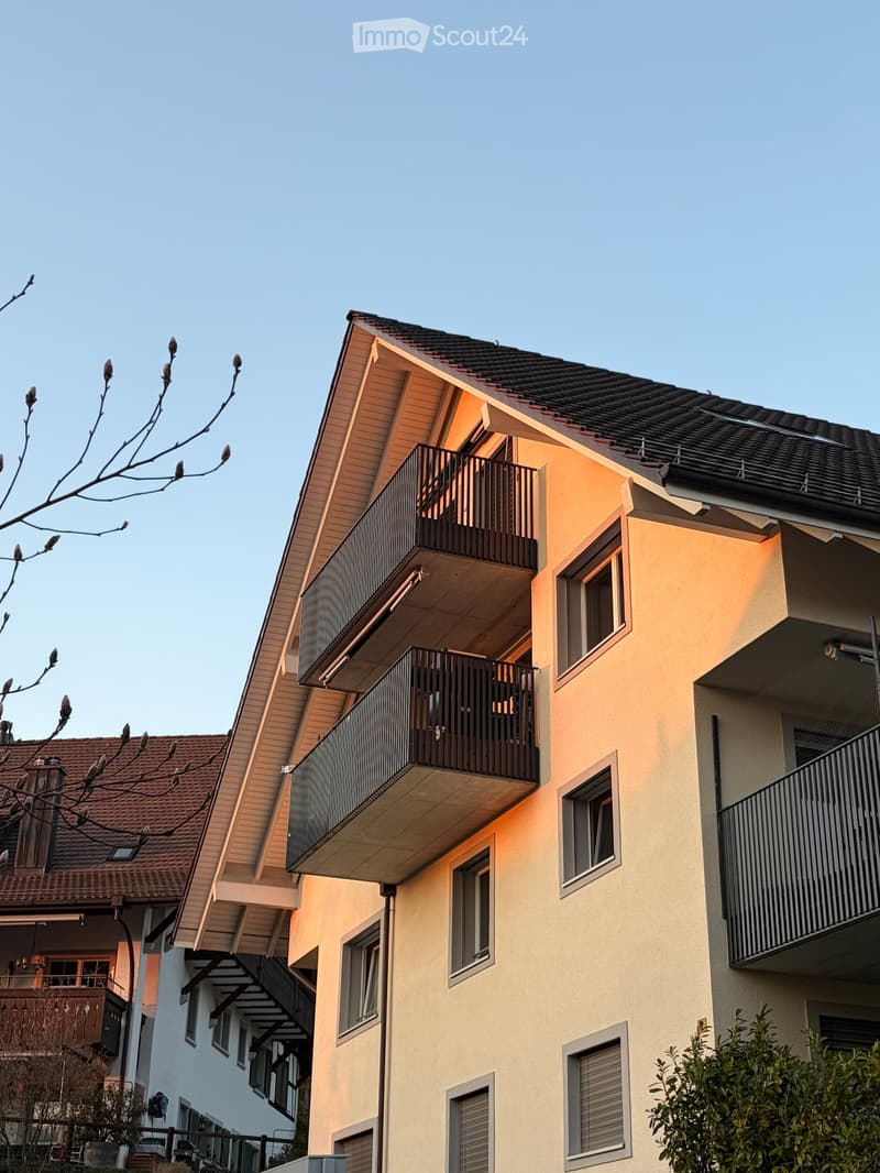 Multi-story residential building with beige facade, multiple balconies, and a dark roof.