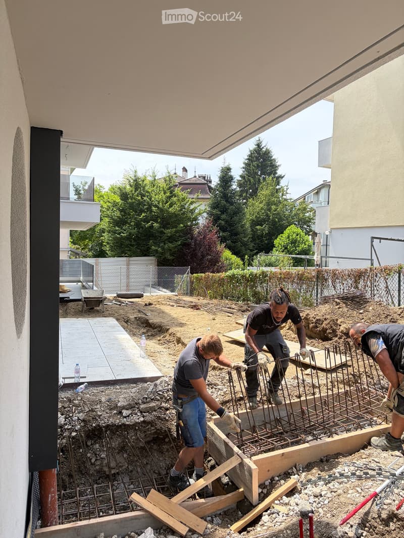 Outdoor construction site with three workers assembling a metal frame structure, surrounded by dirt, rocks, and construction materials.