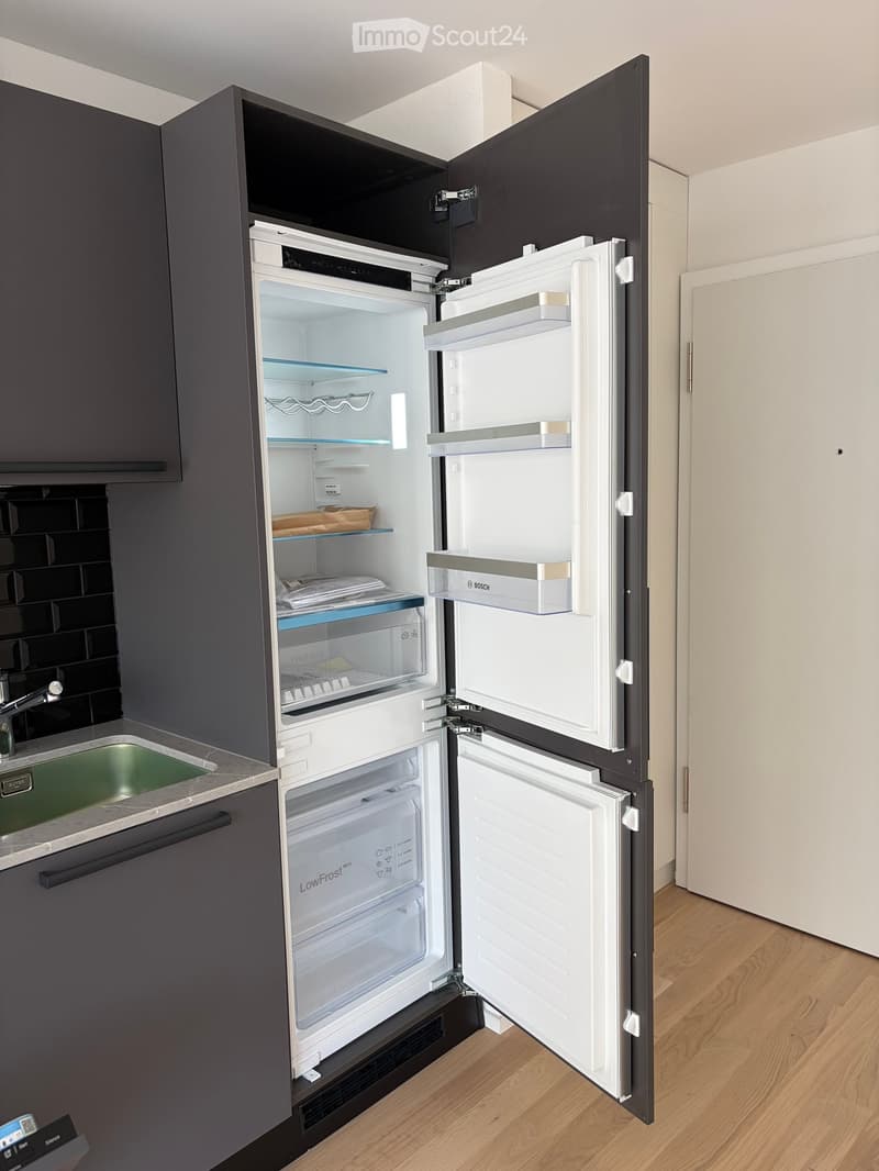 Modern kitchen with dark grey cabinets, a stainless steel sink, and an open refrigerator with multiple compartments.