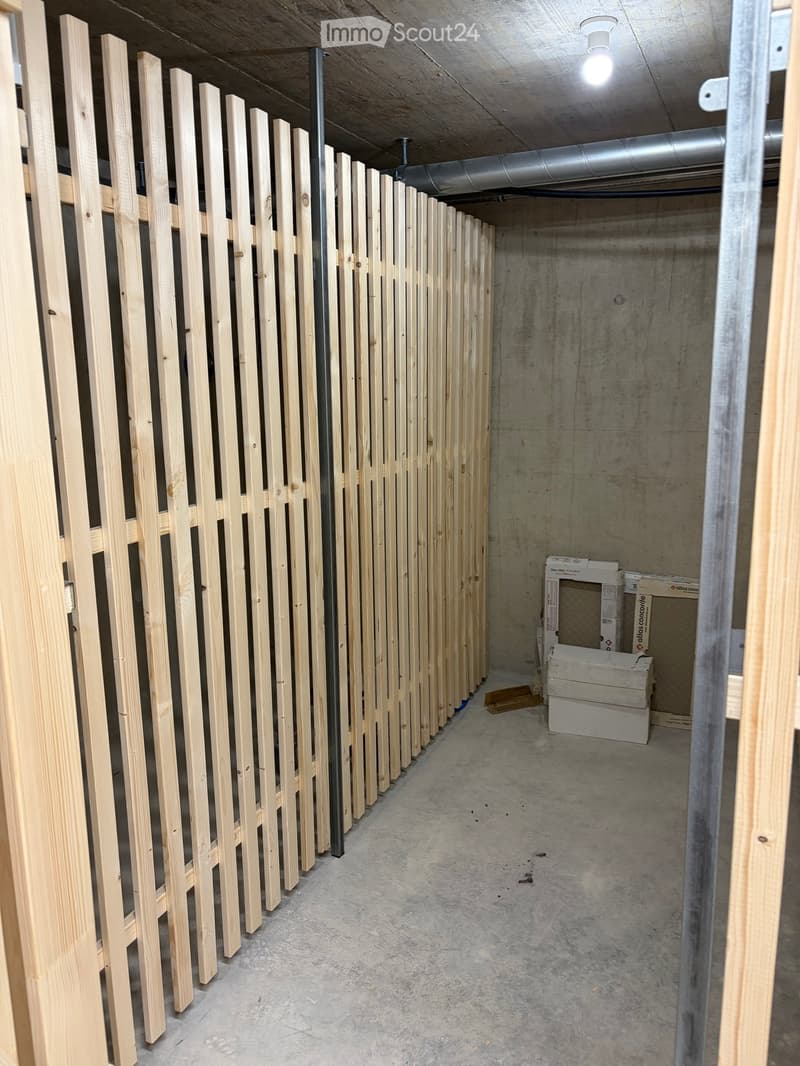 Empty hallway with wooden paneling on one side and concrete walls on the other, featuring a central metal pipe and scattered boxes.