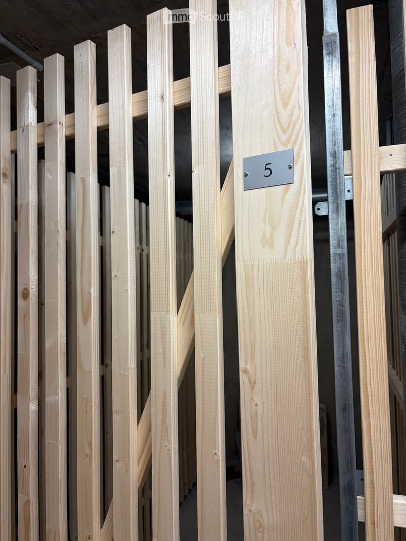 Wooden fence with vertical slats and a metal plaque displaying the number 5, set in a dimly lit indoor space with visible structural beams and pipes.