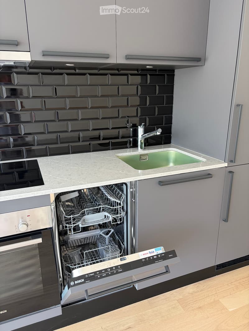 Modern kitchen with stainless steel appliances, black tiled backsplash, and a marble countertop.