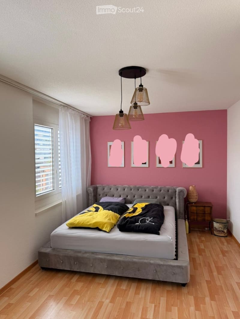 A modern bedroom with a grey upholstered bed, yellow and black duvet, wooden nightstand, and pink accent wall with framed artwork.