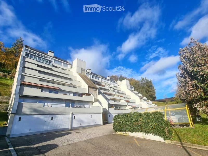 Modern multi-story apartment building with balconies, garage, and parking area.