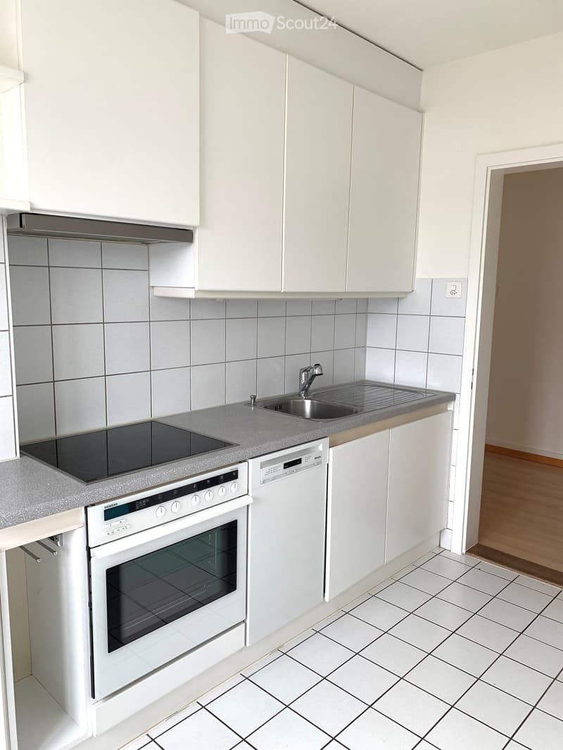 Modern kitchen with white cabinets, tiled walls, and grey countertops. Features an oven, dishwasher, induction cooktop, and sink with a faucet.