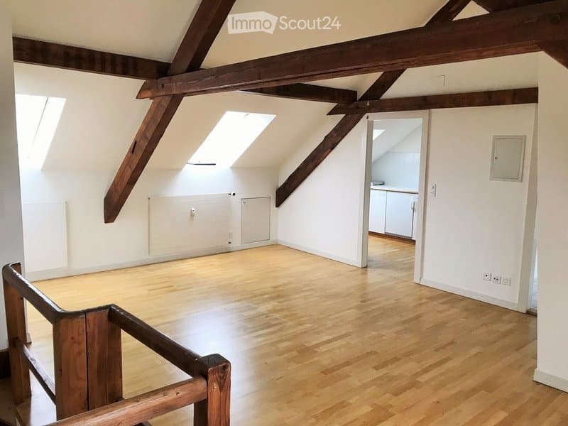 Empty attic room with wooden beams, wooden flooring, and skylights. No furniture or equipment present.