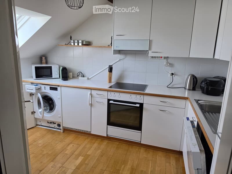 Modern kitchen with white cabinets, wooden countertops, and various appliances including a microwave, oven, washing machine, and induction stove.