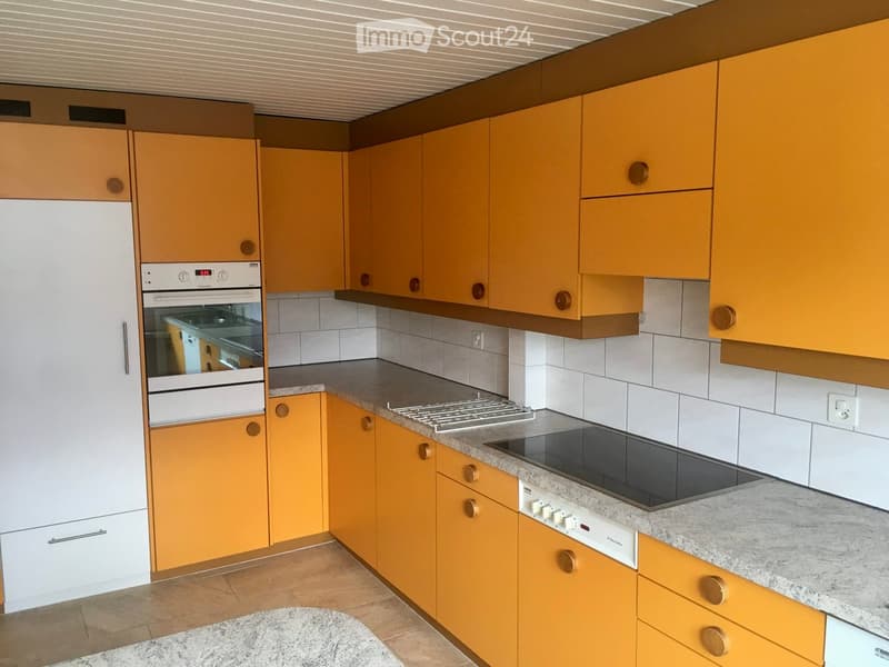 Modern kitchen with orange cabinets, white tiles, granite countertop, built-in oven, and electric stove.
