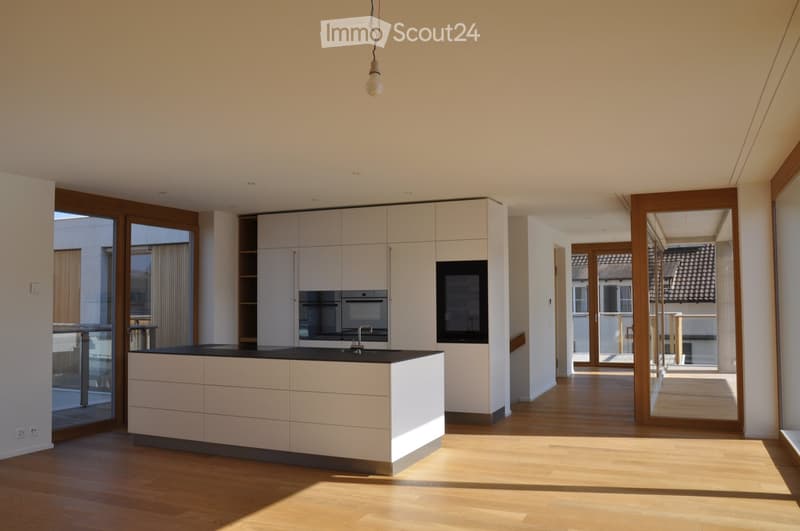 Modern kitchen with white cabinets, black countertop, and integrated appliances, featuring large windows and wooden flooring.