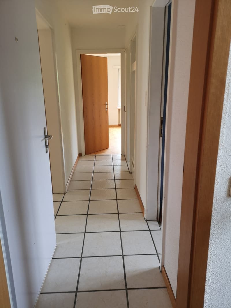 Empty hallway with tiled floor, white walls, and a wooden door at the end.
