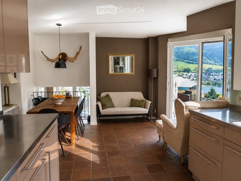 Open-plan living and dining area with a sofa, dining table, chairs, armchair, and a view of a scenic landscape through large windows.