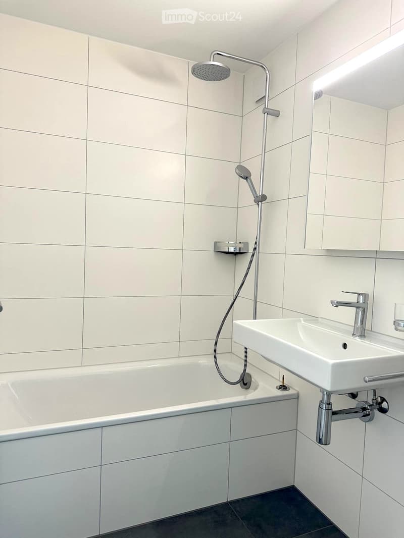 Modern bathroom with white tiled walls, a bathtub, a sink with a chrome faucet, and a handheld showerhead.