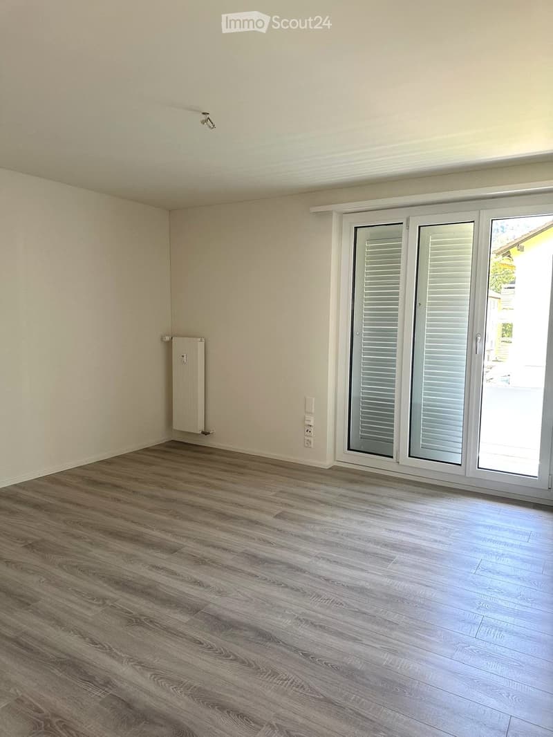 Empty room with wooden flooring, white walls, and a large sliding glass door leading outside.