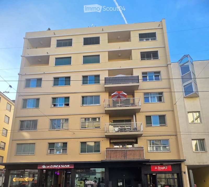 Four-story building with multiple balconies, beige exterior, and commercial storefronts at the bottom.