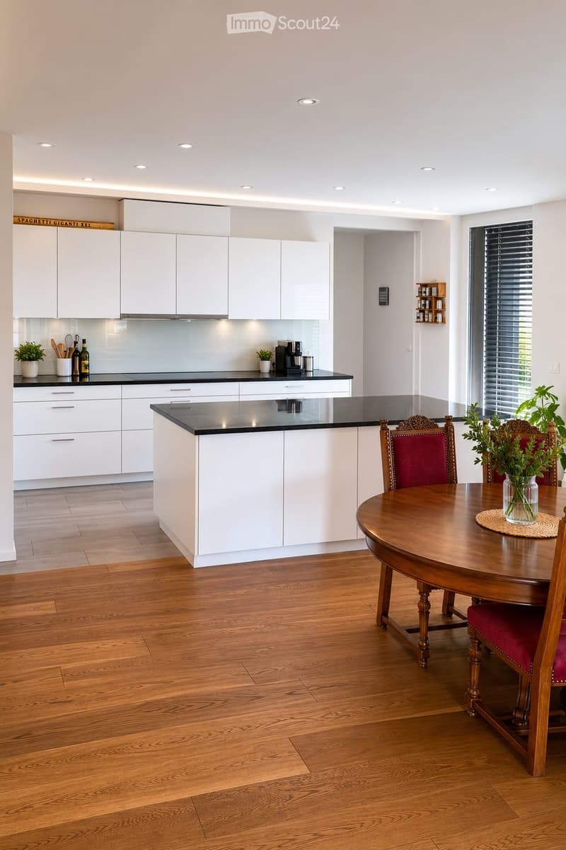 Modern kitchen with white cabinets, black countertops, wooden floor, dining table with chairs, and decorative items.