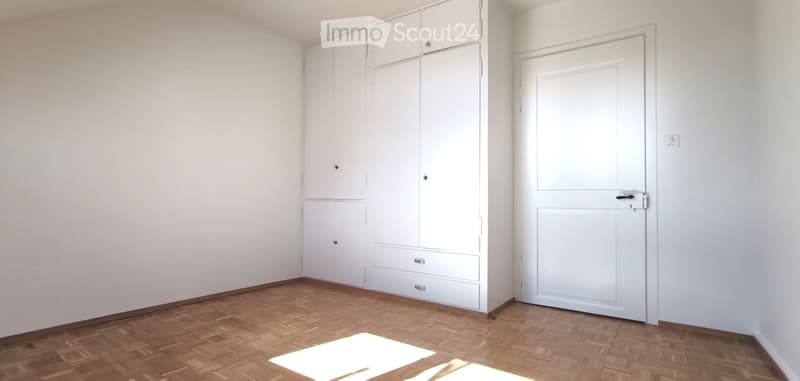 Empty room with white walls, wooden floor, built-in white wardrobe, and a white door.