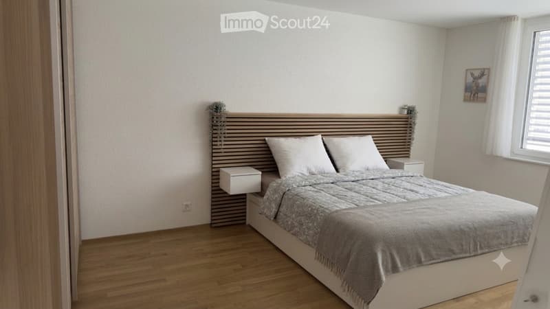 Modern bedroom with a large bed, white pillows, grey bedding, wooden nightstand, and a decorative picture on the wall.